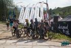 młodzi rowerzyści na tle flag z logotypem Małopolska i namiotów wystawienniczych